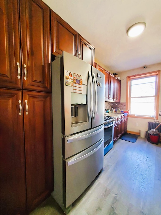 kitchen with stainless steel appliances, a sink, light countertops, backsplash, and light wood finished floors