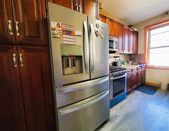 kitchen with a sink, light wood-style floors, light countertops, appliances with stainless steel finishes, and decorative backsplash