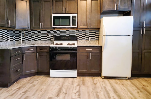 kitchen with dark brown cabinetry, freestanding refrigerator, light wood finished floors, stainless steel microwave, and gas stove