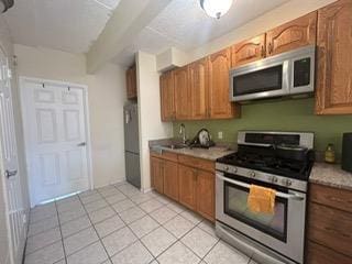 kitchen featuring appliances with stainless steel finishes, sink, light tile patterned floors, and beam ceiling