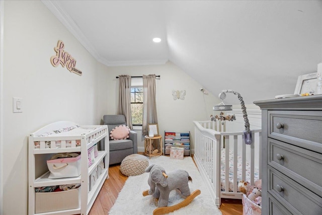 bedroom featuring a crib, ornamental molding, vaulted ceiling, and light wood-type flooring