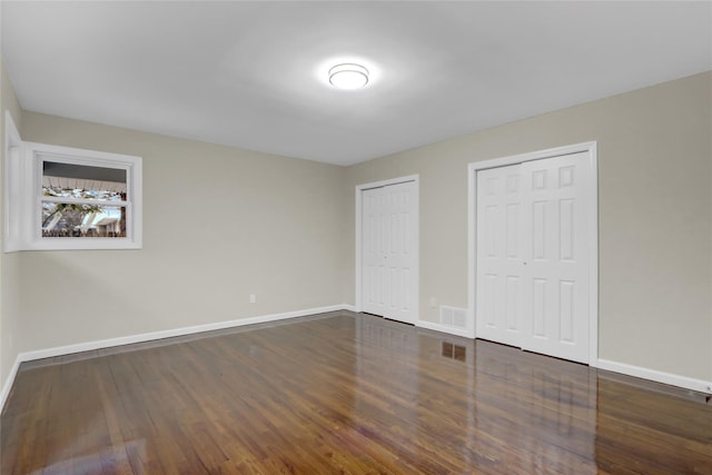 unfurnished bedroom with two closets and dark wood-type flooring