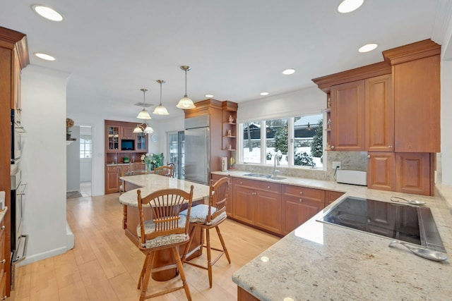 kitchen featuring a breakfast bar, pendant lighting, stainless steel built in refrigerator, sink, and black electric stovetop