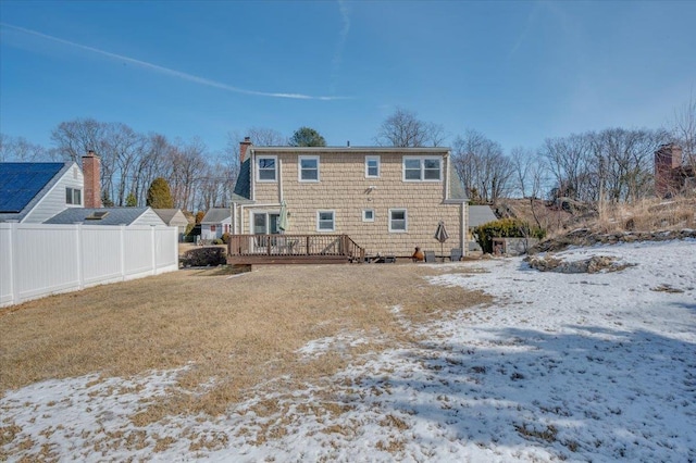 snow covered back of property featuring a deck, a yard, a chimney, and fence