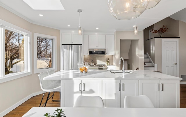 kitchen with appliances with stainless steel finishes, pendant lighting, sink, white cabinets, and a center island with sink