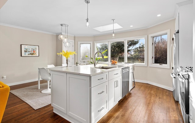 kitchen with sink, an island with sink, pendant lighting, stainless steel appliances, and white cabinets