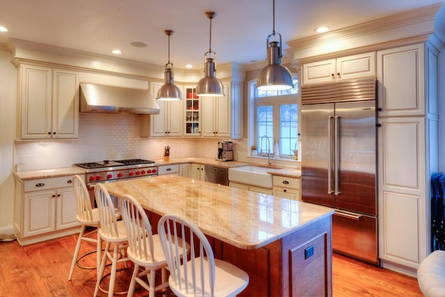 kitchen featuring sink, stainless steel appliances, light stone counters, extractor fan, and a kitchen island