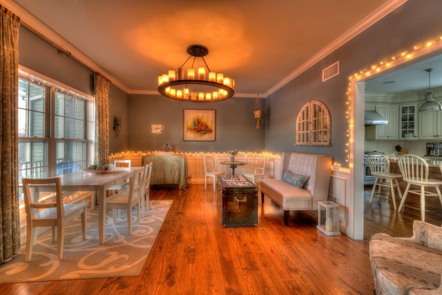 dining space with hardwood / wood-style flooring, ornamental molding, and an inviting chandelier