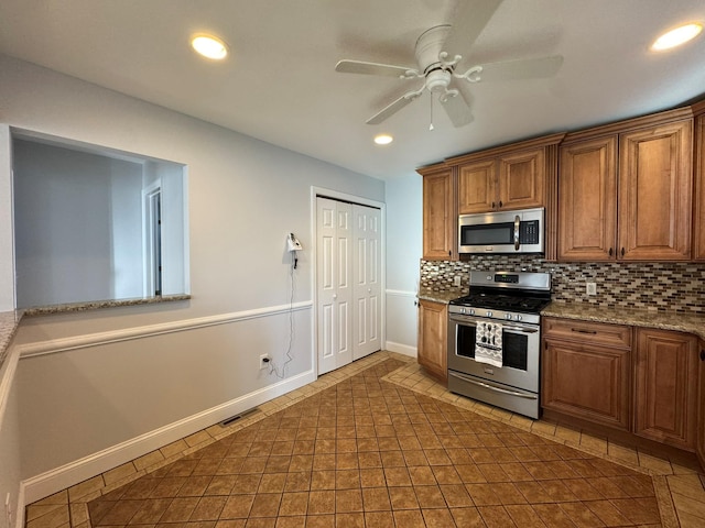 kitchen featuring stainless steel appliances, light stone counters, ceiling fan, backsplash, and dark tile patterned floors