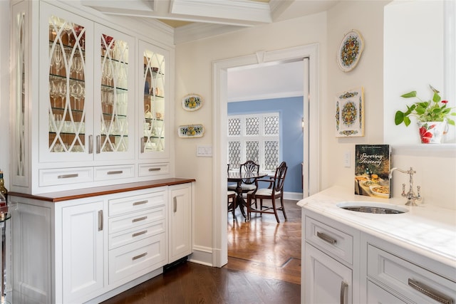 bar with sink, white cabinets, dark hardwood / wood-style flooring, ornamental molding, and light stone countertops