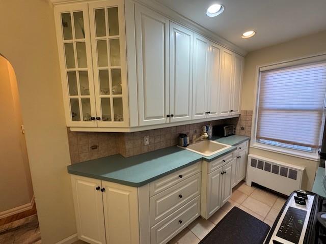 kitchen with radiator heating unit, sink, decorative backsplash, and white cabinets