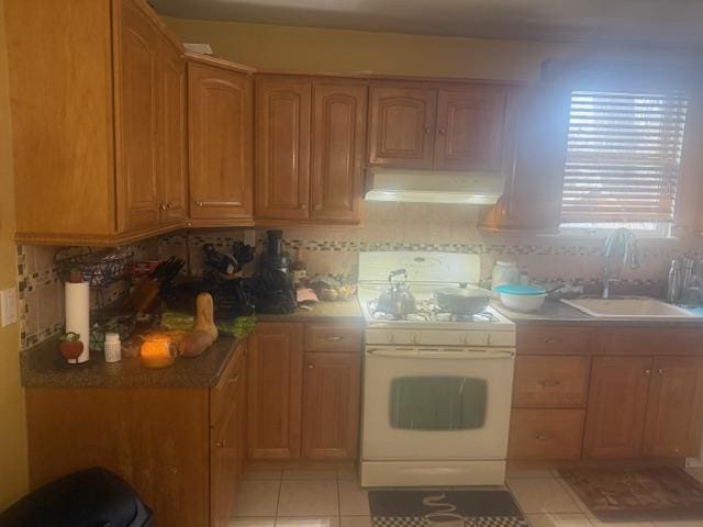 kitchen with tasteful backsplash, light tile patterned flooring, sink, and white range oven