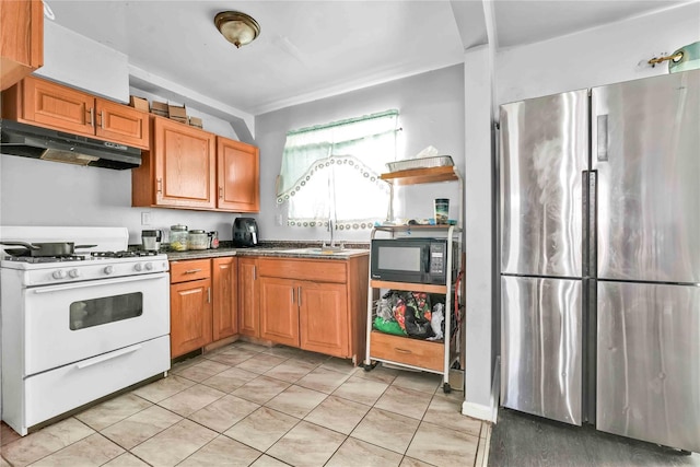 kitchen with stainless steel fridge, white range with gas cooktop, sink, and light tile patterned floors