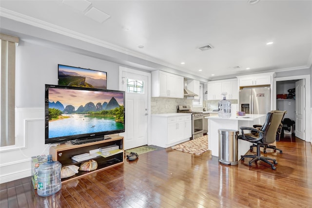 kitchen featuring wall chimney range hood, white cabinetry, stainless steel appliances, a center island, and a kitchen bar