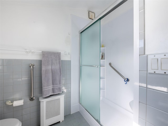 bathroom with tile patterned floors, radiator heating unit, a shower with door, and tile walls