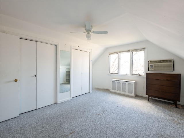 unfurnished bedroom featuring a wall mounted air conditioner, vaulted ceiling, radiator heating unit, carpet floors, and two closets