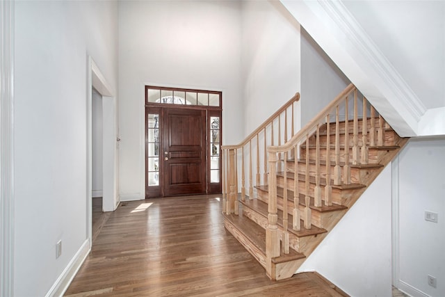 entryway with dark wood finished floors, a towering ceiling, ornamental molding, baseboards, and stairs