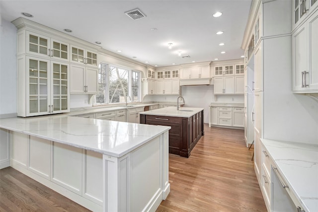 kitchen with glass insert cabinets, a kitchen island with sink, and light stone countertops