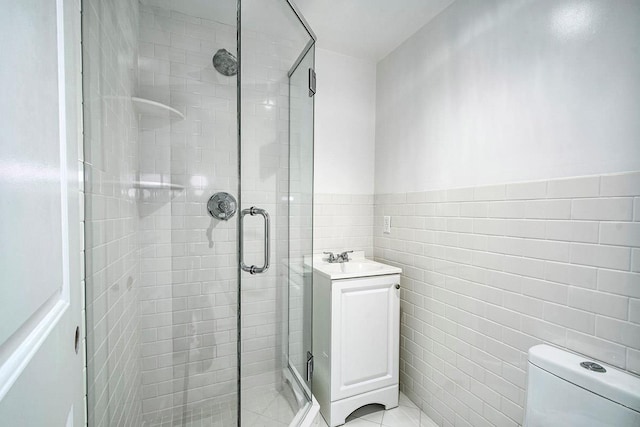 bathroom with a stall shower, toilet, a wainscoted wall, vanity, and tile walls