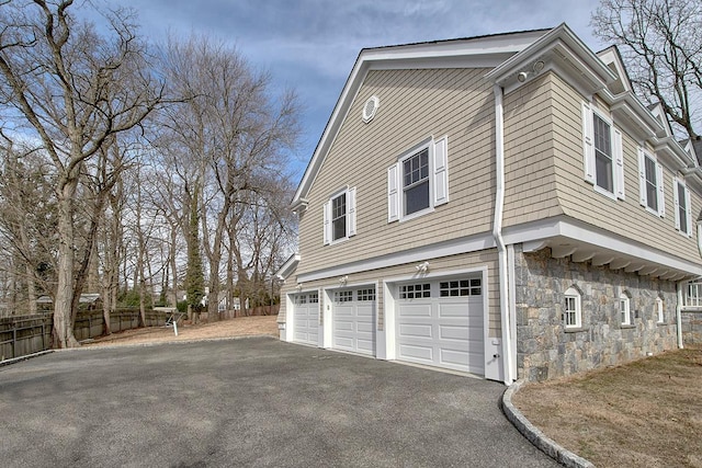 view of property exterior with an attached garage, driveway, stone siding, and fence