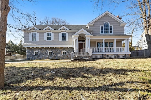 view of front of property with covered porch, fence, a front yard, and stone siding