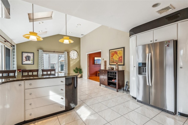 kitchen with lofted ceiling, dark stone countertops, white cabinets, stainless steel fridge with ice dispenser, and decorative light fixtures