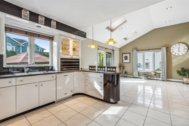 kitchen with sink, white dishwasher, white cabinets, decorative light fixtures, and dark stone counters