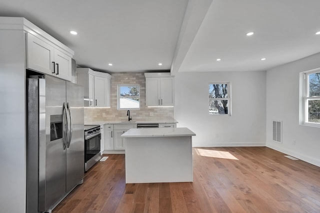 kitchen with a kitchen island, appliances with stainless steel finishes, sink, white cabinets, and backsplash