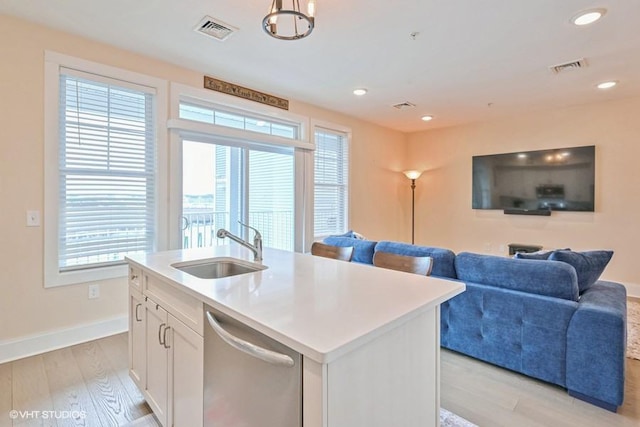 kitchen featuring sink, white cabinetry, light hardwood / wood-style flooring, stainless steel dishwasher, and an island with sink