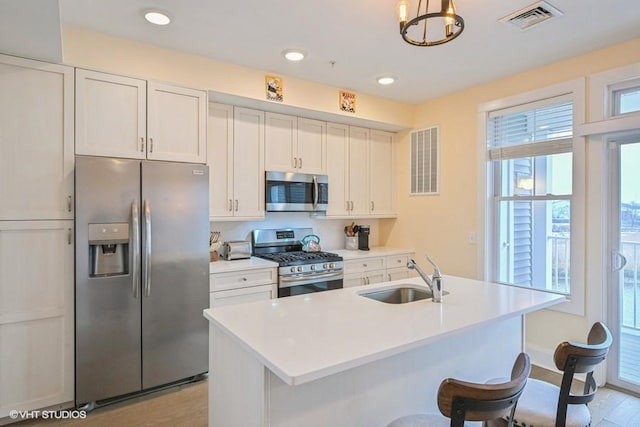 kitchen featuring sink, a center island with sink, appliances with stainless steel finishes, pendant lighting, and white cabinets