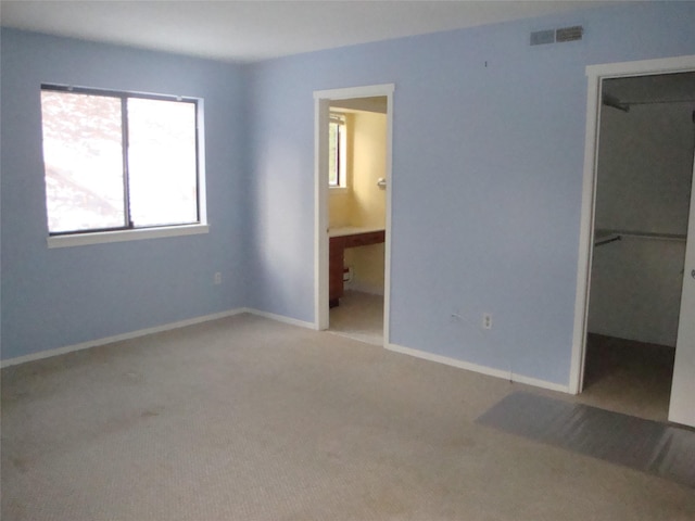 unfurnished bedroom with a walk in closet, ensuite bathroom, light colored carpet, and a closet