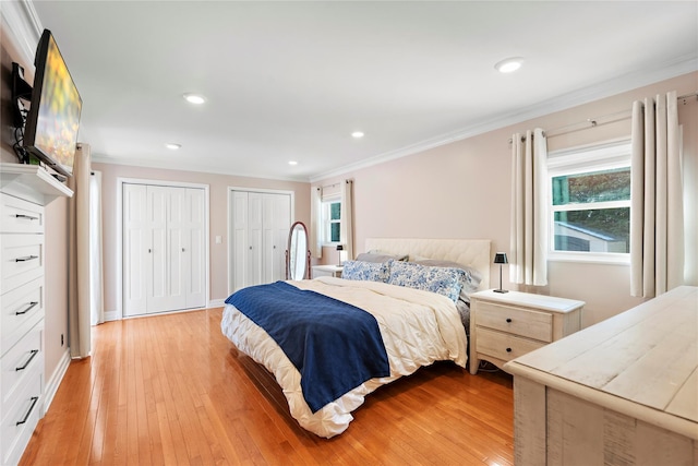 bedroom with ornamental molding, light hardwood / wood-style floors, and multiple closets