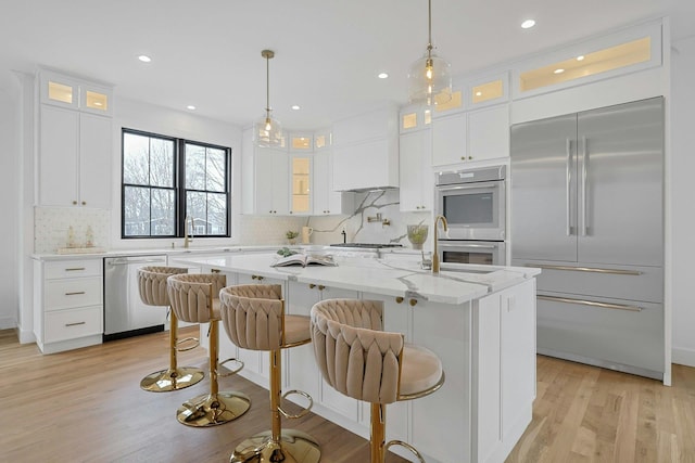 kitchen with white cabinets, glass insert cabinets, decorative light fixtures, a kitchen island with sink, and stainless steel appliances