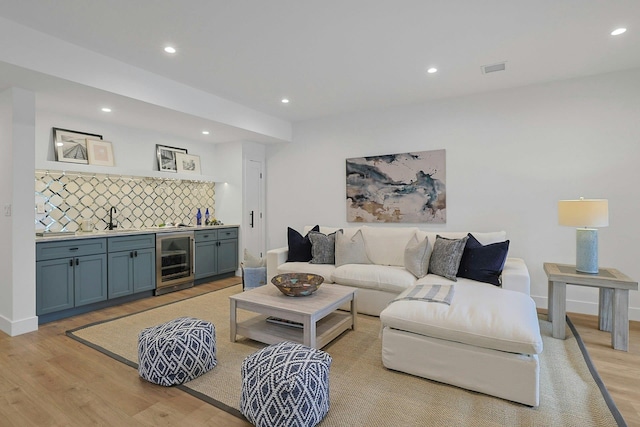 living room featuring beverage cooler, baseboards, light wood-style floors, indoor wet bar, and recessed lighting