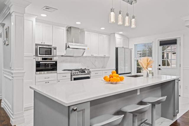 kitchen featuring stainless steel appliances, a center island with sink, white cabinets, and wall chimney exhaust hood