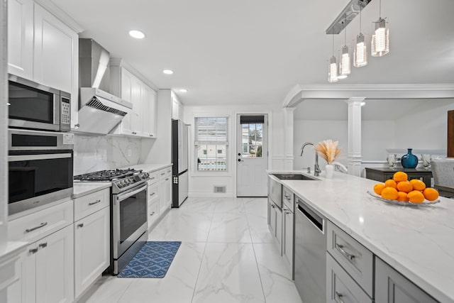 kitchen with sink, stainless steel appliances, light stone countertops, white cabinets, and wall chimney exhaust hood