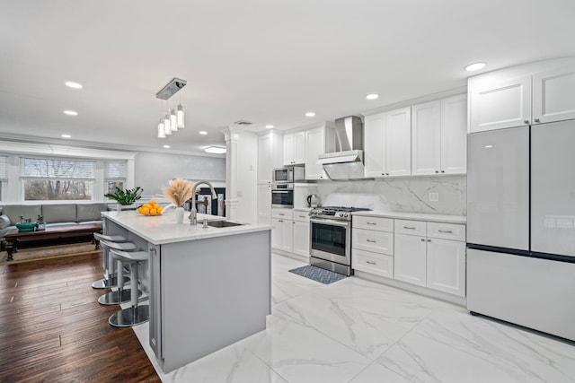 kitchen featuring appliances with stainless steel finishes, pendant lighting, white cabinetry, sink, and wall chimney exhaust hood