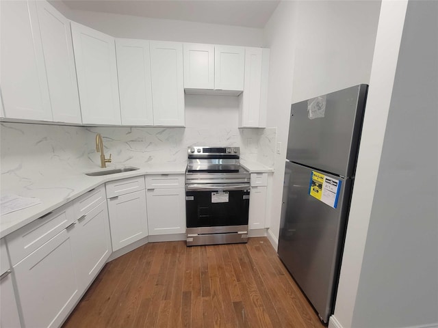 kitchen with appliances with stainless steel finishes, tasteful backsplash, sink, white cabinets, and hardwood / wood-style flooring