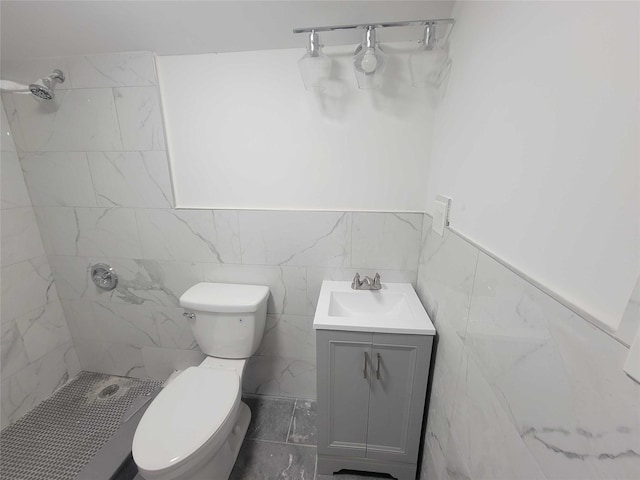 bathroom with vanity, a tile shower, tile walls, and toilet