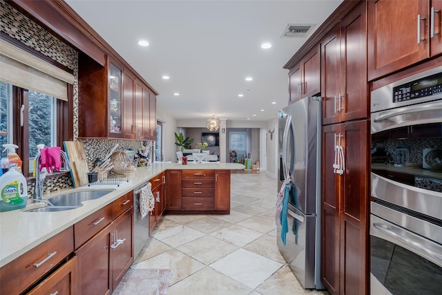 kitchen featuring sink, light tile patterned floors, appliances with stainless steel finishes, backsplash, and kitchen peninsula