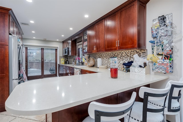 kitchen featuring decorative backsplash, stainless steel appliances, kitchen peninsula, and a kitchen bar