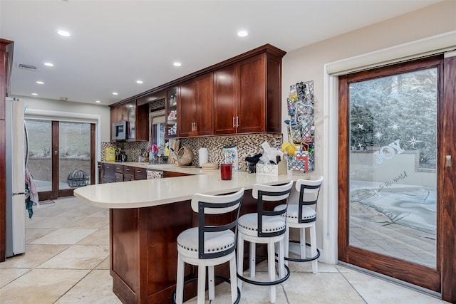 kitchen featuring a breakfast bar, appliances with stainless steel finishes, tasteful backsplash, a healthy amount of sunlight, and kitchen peninsula