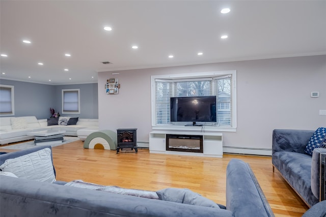 living room with a baseboard heating unit, crown molding, light hardwood / wood-style floors, and a wood stove