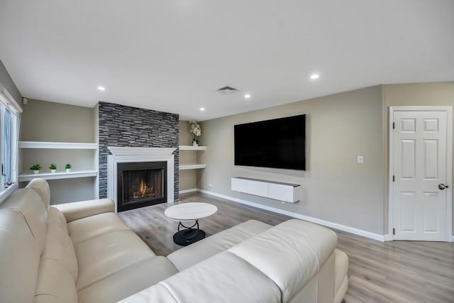 living room with built in features, a fireplace, and light hardwood / wood-style flooring