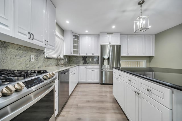 kitchen featuring appliances with stainless steel finishes, white cabinetry, sink, hanging light fixtures, and light hardwood / wood-style flooring