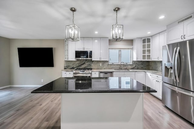 kitchen featuring pendant lighting, appliances with stainless steel finishes, white cabinets, a kitchen island, and dark stone counters