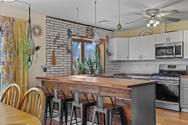 kitchen featuring white cabinetry, butcher block countertops, stainless steel appliances, and a kitchen bar