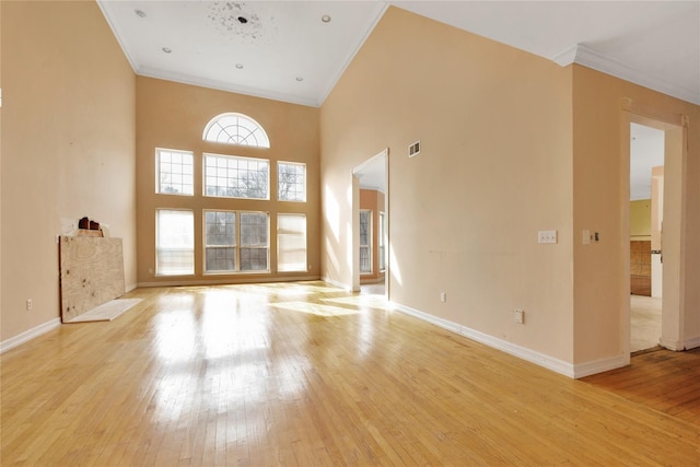 unfurnished living room with crown molding, a towering ceiling, and light wood-type flooring