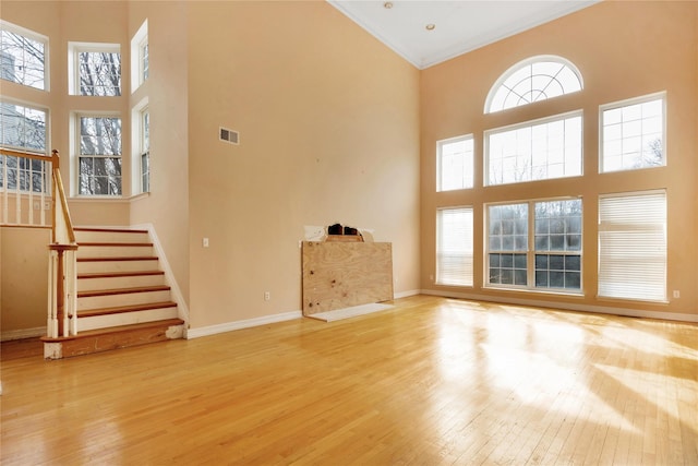 unfurnished living room featuring a wealth of natural light, light wood-type flooring, and a high ceiling