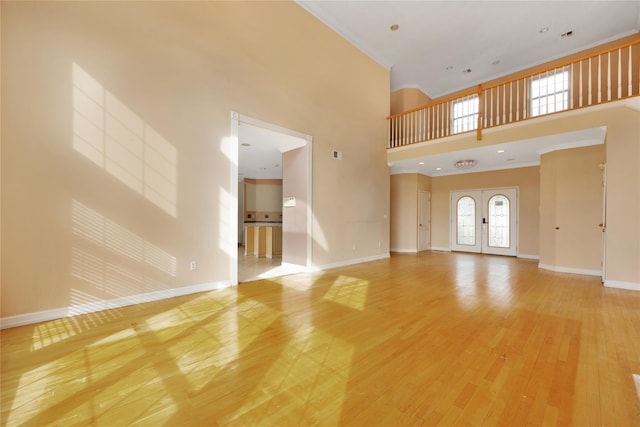 unfurnished living room with crown molding, a towering ceiling, wood-type flooring, and french doors